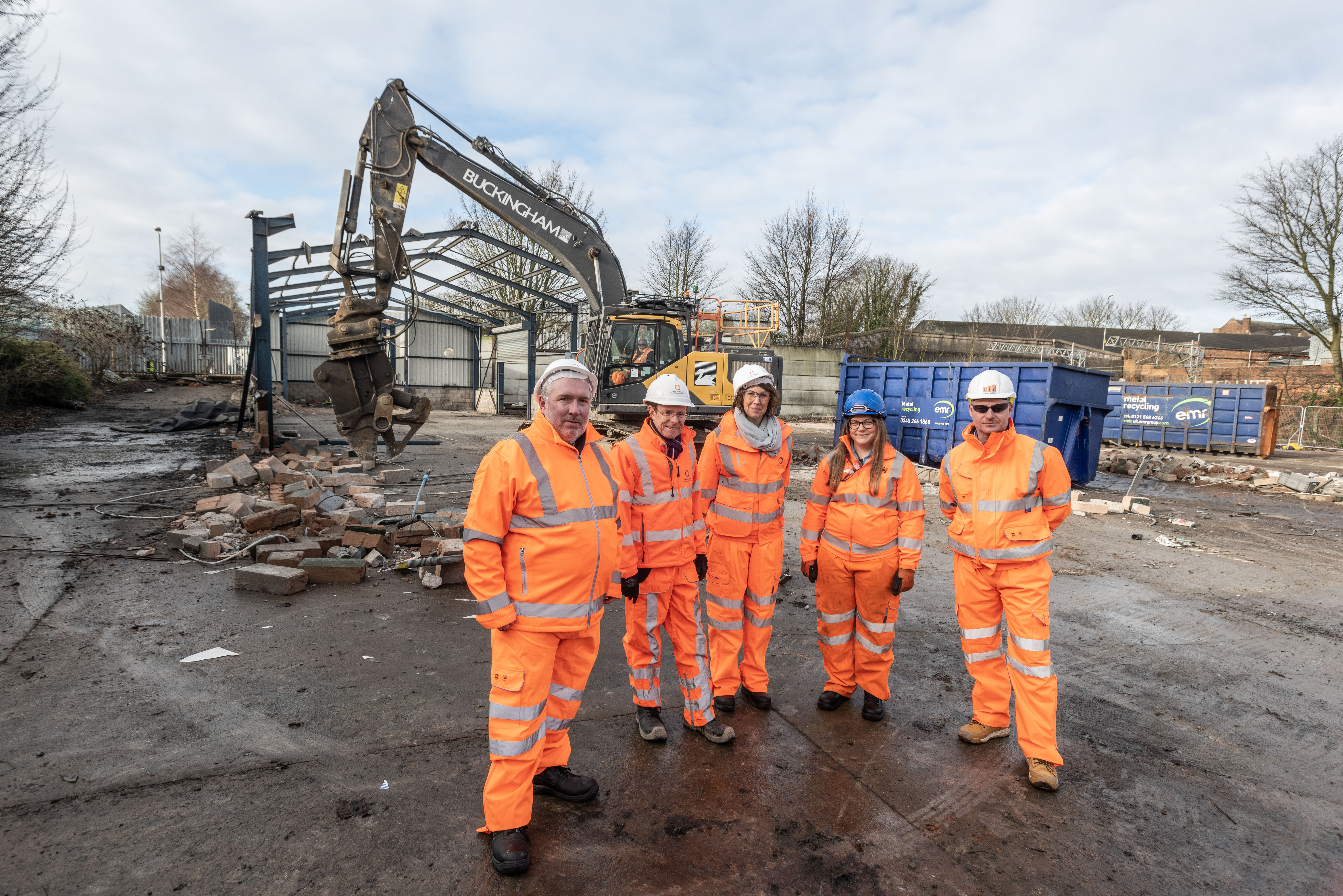 Rail bosses overlooking site with digger and frame of industrial unit being demolished