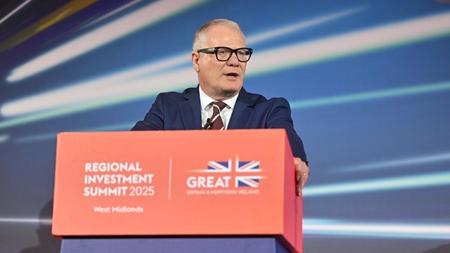 A speaker at the Regional Investment Summit 2025 in West Midlands stands at a podium decorated with a British flag backdrop.