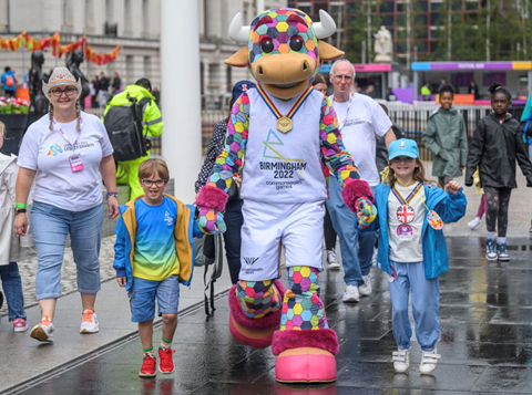 People walking hand in hand wearing Birmingham 2022 merchandise alongside Games' mascot Perry the Bull 